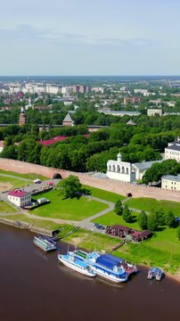Vertical video. Veliky Novgorod, Russia. Novgorod Kremlin (Detinets) with golden-domed cathedrals and 15th-century stone walls, Drone footage over the Volkhov River on a bright summer day.. Drone foo