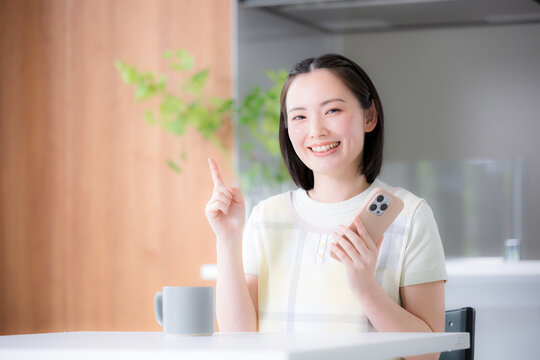 スマートフォンを持ってポイントポーズの主婦のようなエプロンを着た女性　家事代行、時短や節約などの消費者、前向きポジティブイメージ