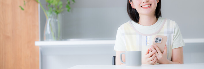 主婦のようなエプロンを着た女性　スマホを持って検索や探す比較する、口コミの投稿などキッチンやダイニングでくつろぐ　顔無しのバナー © kapinon