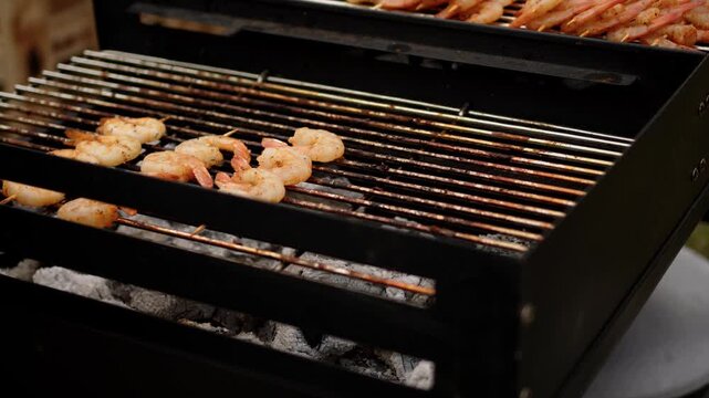 Shrimp cooking on a charcoal grill. Seafood skewer roasting over hot coals for an outdoor summer barbecue party. Gourmet meal preparation in professional kitchen.