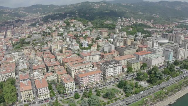 La Spezia, Italy. Aerial flight along Viale Italia embankment, terracotta rooftops, deep-water harbor with a large cruise ship docked under clear summer skies.. Drone footage