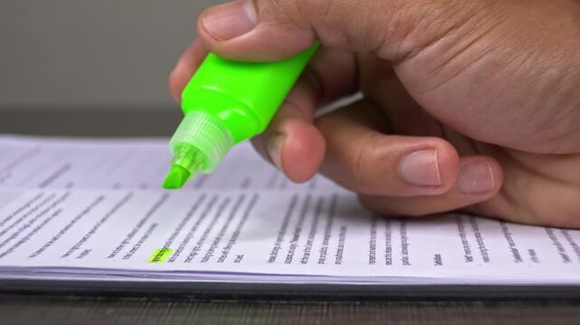 Hand using a neon green marker to highlight important text on a document close-up view