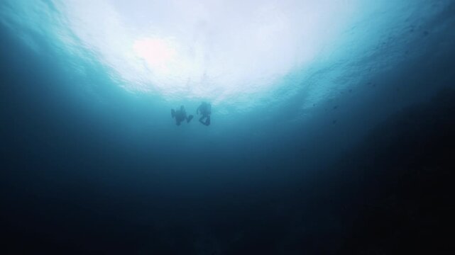 Group of scuba divers cinematic silhouettes in bright sun light beams swims underwater Slow motion, Wreck diving. Mediterranean sea, Cyprus. Active sport, diving concept. Deep ocean blue water