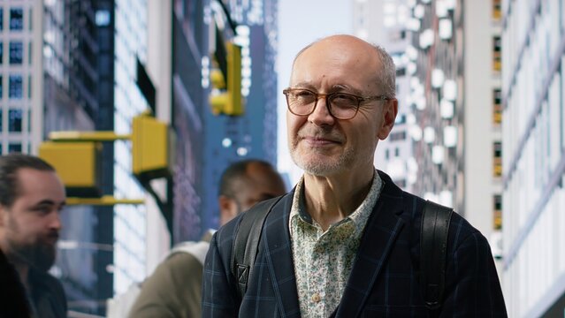 Street portrait of elderly male business professional with glasses among urban crowd, highlighting movement, activity and diverse pedestrians in a busy downtown cityscape. Retirement age. Camera B.