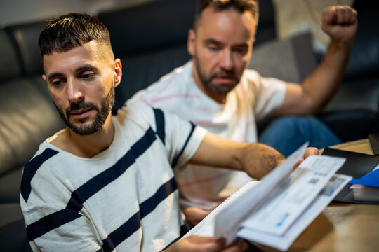 Emotional gay couple fighting over money and bills on sofa.