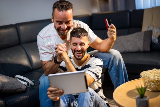 Joyful same sex couple making a high five while shopping online with a tablet and card.