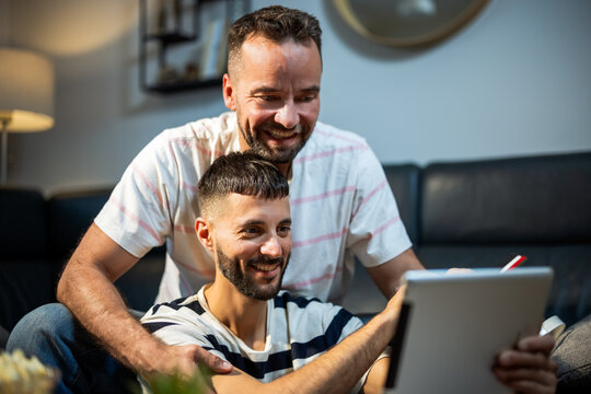 A cheerful same sex couple using a digital tablet and credit card to shop online at home.