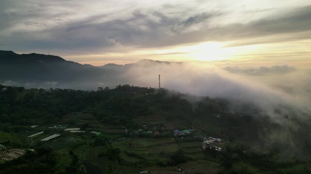 Picturesque aerial drone shot of mountain landscape with rolling fog and warm sunrise light over rural Benguet Province, Philippines.