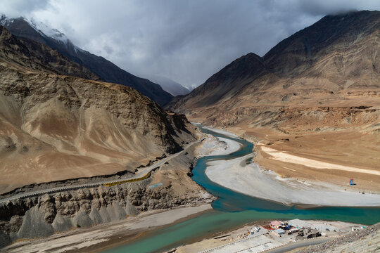 Majestic confluence of Indus and Zanskar rivers in Ladakh, India. Dramatic mountain landscape with winding turquoise water under cloudy sky. Famous Sangam viewpoint in Himalayan high altitude desert.