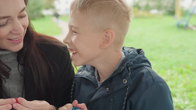 Mother tending son before back to school, closeup application of sticker on nose, gentle reassuring touch and smile, outdoor green background with bench and jacket, intimate bonding scene showing