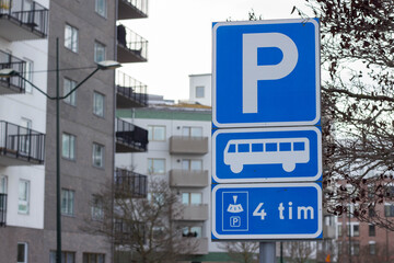 Fototapeta premium Blue parking sign indicating bus parking with time limit, residential buildings in the background, balconies visible on multiple floors