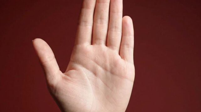 Hand Raised Palm Forward Stop Gesture on Maroon Background