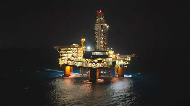 Illuminated offshore oil rig platform operating at night in the ocean.