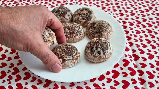 Seven round cookies dusted with cocoa and powdered sugar rest on a white plate atop a red heart patterned tablecloth, presenting a sweet dessert with a festive romantic touch