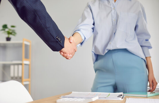 Cropped photo of business woman standing in office on workplace shaking hands with a man colleague reaching agreement making a good deal or signing a contract. Business people at work.