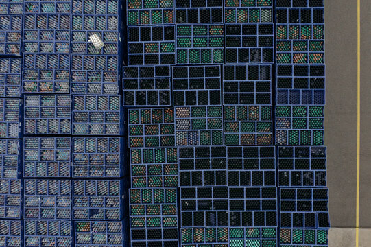 Aerial view of organized stacks of blue plastic crates filled with glass bottles on an asphalt surface in an industrial yard.