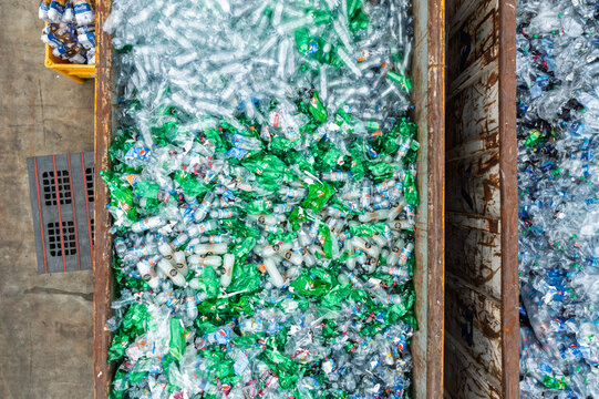 Aerial view of a large metal container filled with thousands of clear and green plastic bottles at a recycling facility.