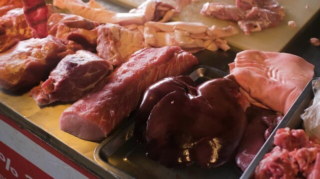 Butcher stall showing assorted raw meat cuts including pork beef and offal arranged on counter at market. Fresh meat selection concept