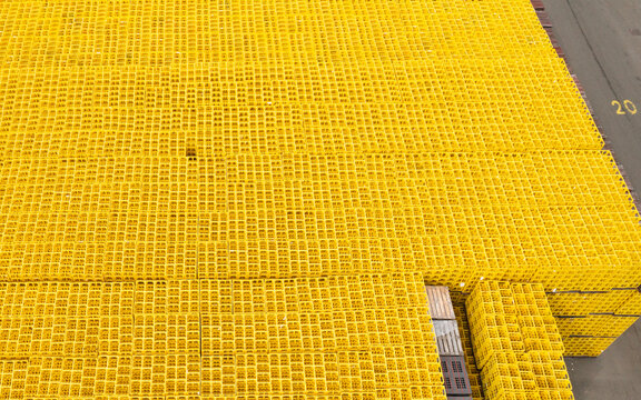 Aerial view of thousands of vibrant yellow plastic beverage crates stacked in a dense grid pattern in an industrial storage yard of a logistics center.
