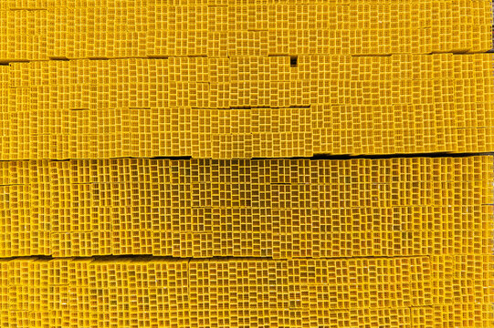 Aerial view of stacked yellow square industrial pipes arranged in a dense grid pattern with repetitive geometric textures.