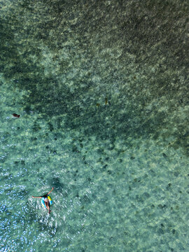 Aerial view of a woman floating on a colorful inflatable ring in clear turquoise tropical water with the seabed visible Guanaja, Bay Islands Department, Honduras.