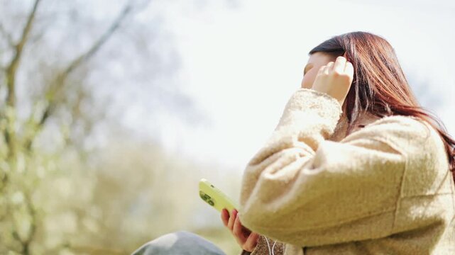Joyful woman connects with music outdoors. Relishing serene moments under sun, smiles listening to favorite tunes through earphones. Embracing nature, finding peace and happiness with personal audio.