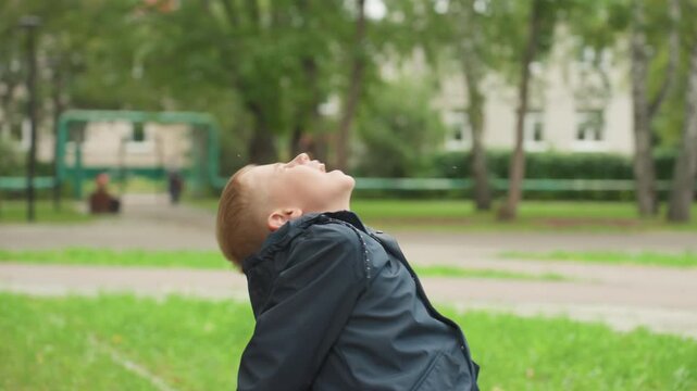 Young white boy holding snack outdoors, small student pauses on park bench while inspecting wrapped cereal, nervous expression and sigh show back to school jitters, damp overcast morning with green