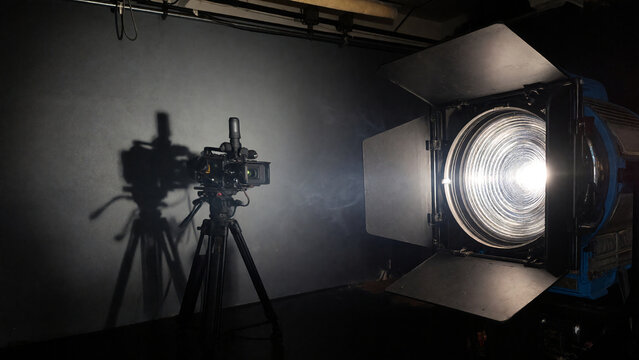 Cinematic close-up of a professional studio fresnel light with barn doors, emitting a powerful beam of cool white light.j