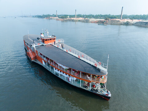 Aerial view of a Sadarghat passenger ferry with people on deck cruising on the Buriganga River under a hazy sky in Dhaka, Dhaka Division, Bangladesh.