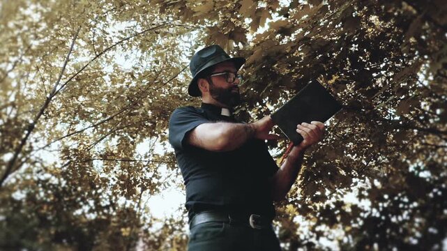 Religious man, reverend or priest wearing a clerical collar and holding a bible. Preacher preaching the gospel in a rural setting.
