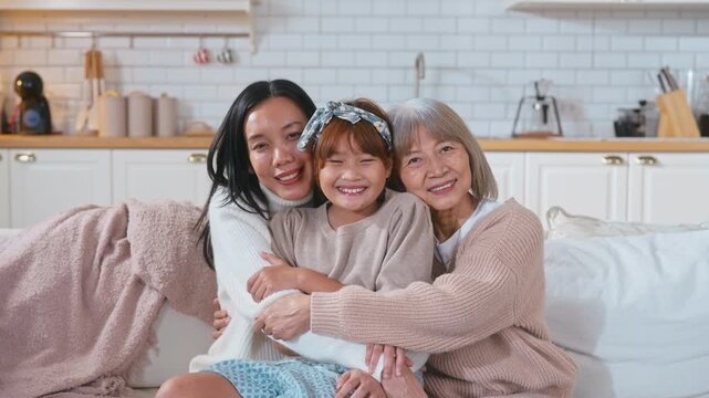 Portrait of three generations of Asian women a cute little girl hugging her mother and grandmother while smiling and enjoying quality family time together at home bonding with love, care, affection