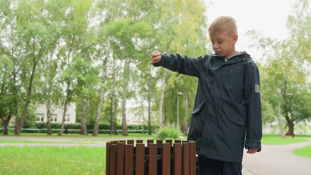 Boy respectfully throws trash away. Young boy properly disposes of wrapper thoughtfully. Conscientious boy demonstrates civic pride by carefully disposing of his trash responsibly in park