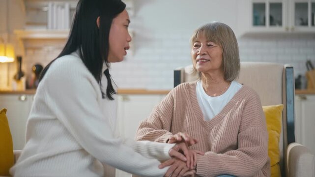 Elderly Asian mother is hugging and lovingly comforting her daughter on a sofa. She is listening and providing emotional support and encouragement in a warm, cozy living room at home together.