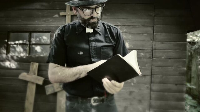 Clergyman, reverend or priest wearing a clerical collar and reading a bible. Preacher preaching the gospel in front of an old rustic rural church.