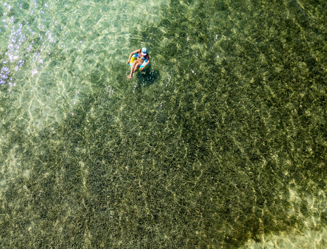Aerial view of a woman floating on an inflatable ring in the clear turquoise water of Guanaja, Bay Islands Department, Honduras.