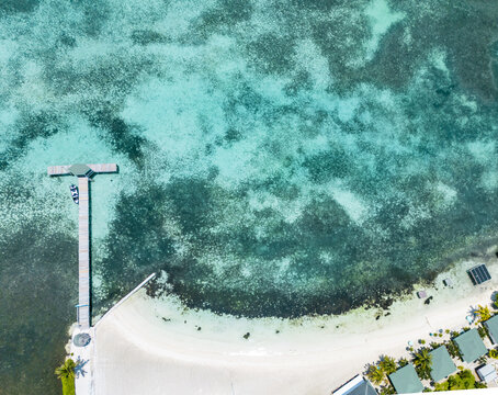 Aerial view of a wooden T-shaped pier stretching into turquoise Caribbean waters with coral reefs and a white sandy beach in Guanaja, Bay Islands Department, Honduras.