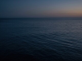 Fototapeta premium Tranquil expanse of the open ocean at dusk, where the deep blue water meets the fading horizon under a vast, silent sky, conveying solitude and natural beauty