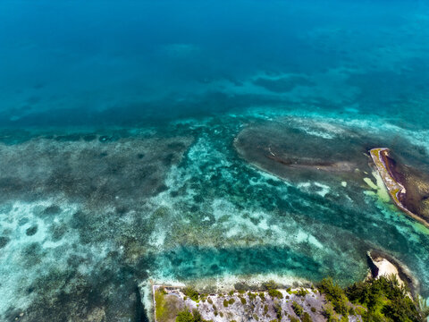 Aerial view of the vibrant turquoise coral reefs and crystal clear waters along the lush coastline of Guanaja, Bay Islands Department, Honduras.
