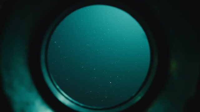 Looking through a submarine periscope at the deep blue ocean water with tiny particles floating in the mysterious underwater environment