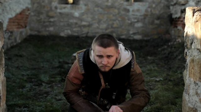 Medieval warrior in leather armor kneeling and smelling the ground inside ancient stone fortress ruins. Cinematic tracker scene &mdash; dramatic historical reenactment footage for action and history content