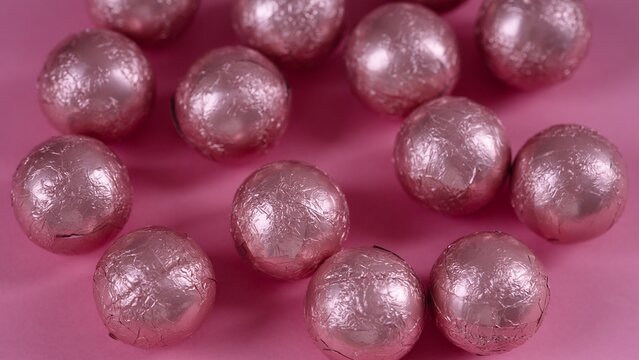 Close-up shot of a group of chocolate candy balls wrapped in pink foil on a pink background.