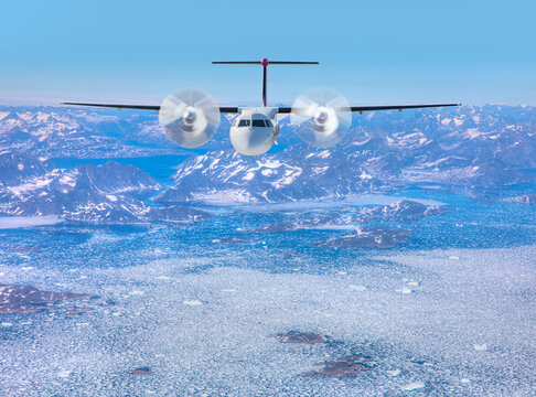 White metallic propeller passenger airplane in the sky - View from airplane of melting polar ice cap and snowy mountains - Greenland
