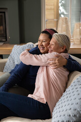 Naklejka premium Diverse female friends wearing sweater and blouse sitting on living room sofa, hugging with pillows