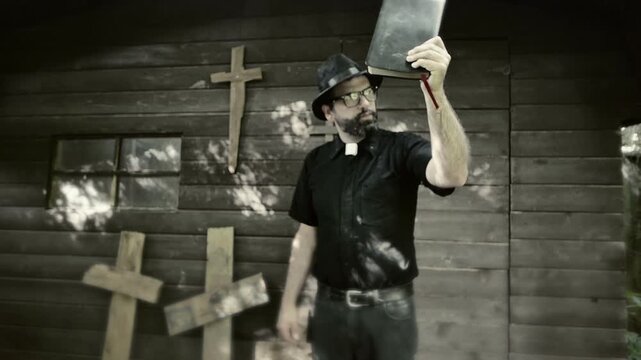 Clergyman, reverend or priest wearing a clerical collar and holding up a bible. Preacher preaching the gospel in front of an old rustic rural church.