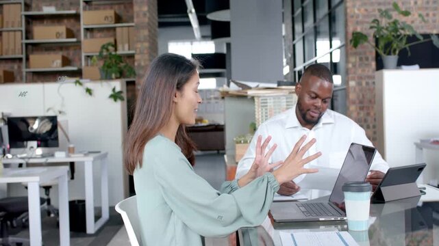 Seated woman starting discussion widening gestures man discussing documents on laptop in business