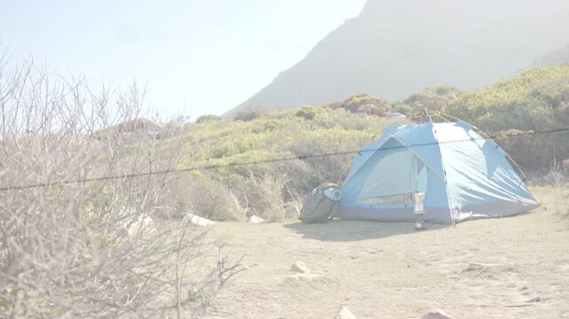 Blue tent staying in sunlit outdoor campsite, thin wire crossing near lens and shifting exposure