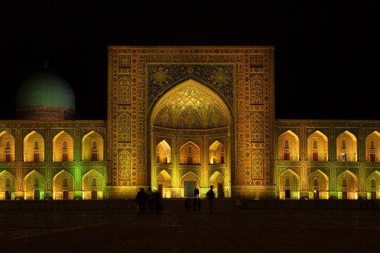 Illuminated Tilla-Kari madrasah facade at Registan Square in Samarkand at night with intricate tilework and turquoise dome. Ideal for travel publications and heritage content.