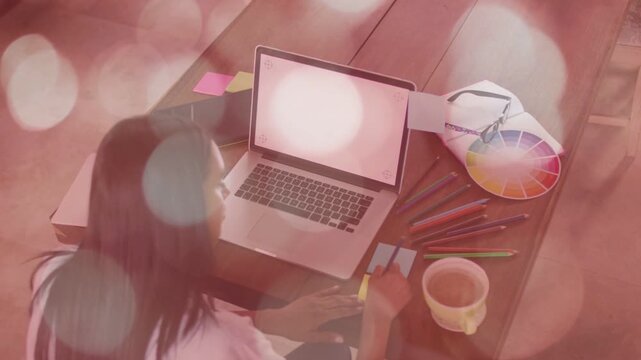 Woman designer planning, reaching yellow tab, aligning notes on laptop, bokeh overlay appearing