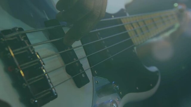 Bassist's right hand hovering pickups, starting string plucks and rolls, driving music amid bokeh