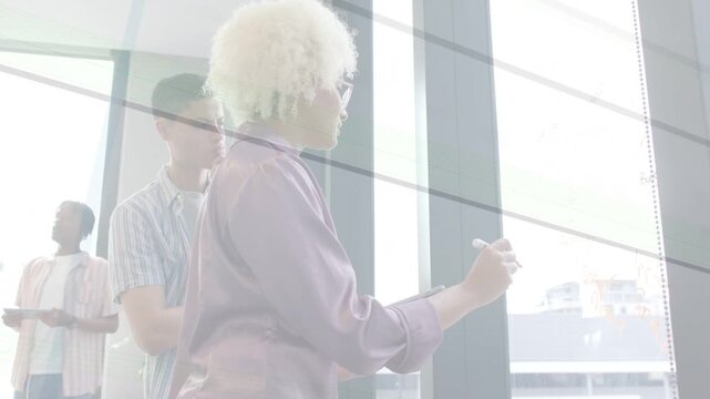 Facilitator stepping to glass, writing and animating business plan charts while teammate leaning in